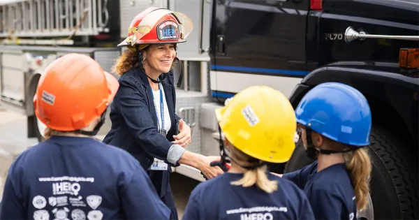 President Berne, wearing a firefighter helmet, shakes hands with young girls in the CampHero program.