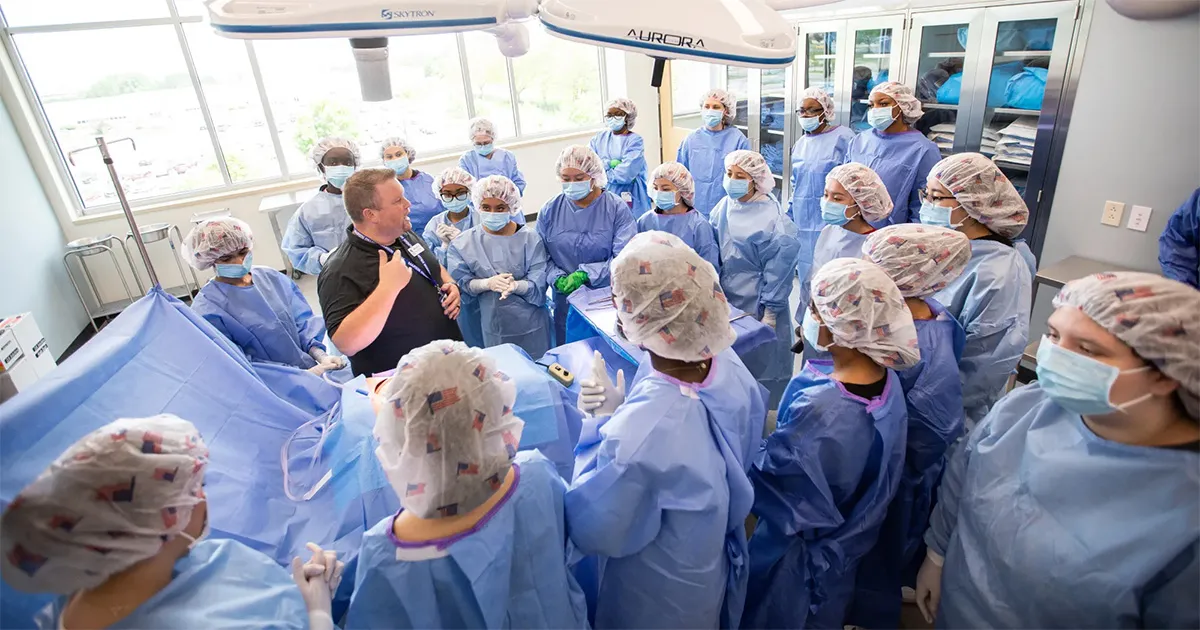 Group of students dressed in surgical gowns listening to instructor